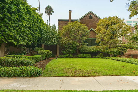 Front view of a house with a gabled roof and a chimney, surrounded by trees and shrubs.