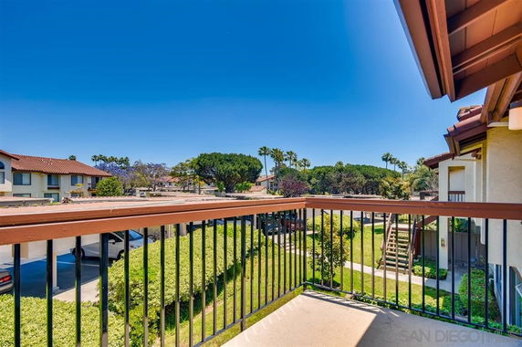 View from a balcony overlooking a residential area with greenery and neighboring buildings.