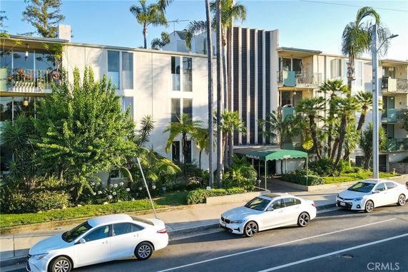 Front view of a multi-story residential building with balconies and surrounding palm trees.