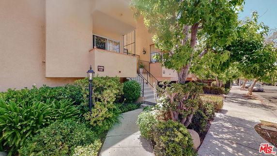Front view of a multi-unit residential building with a small staircase and shrubbery.