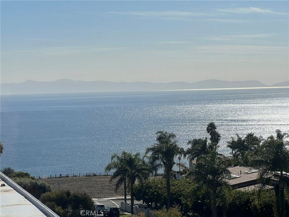 Panoramic view of an ocean with distant mountains and a foreground featuring trees and rooftops.
