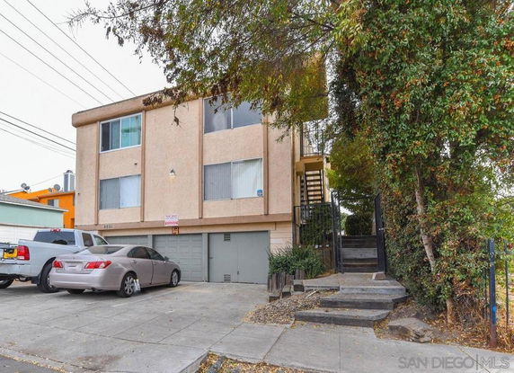 Front view of a multi-story apartment building with a driveway and parked cars.