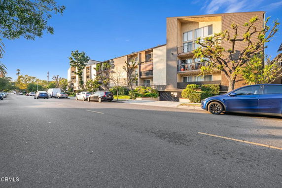 Front view of a multi-story apartment building with balconies and parking in front.