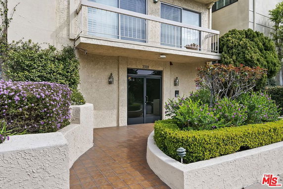 Front view of a multi-story residential building with plants and a walkway.