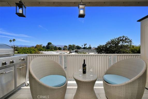 Outdoor balcony with a grill, two chairs, and a table set up for drinks, overlooking distant trees and mountains.