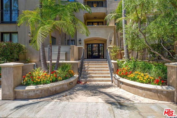 Front view of a multi-story building entrance with stairs and landscaped gardens.