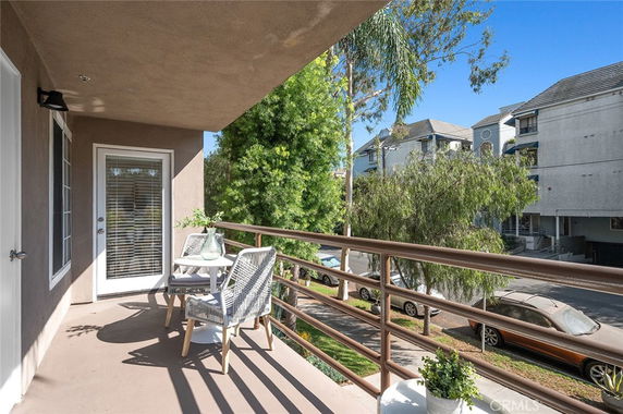 View of a balcony with a table and chairs, overlooking a street with trees and buildings.