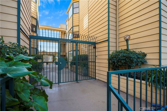 Front view of a gated building entrance with yellow siding and green metal fencing.