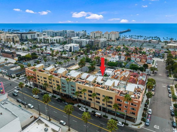 Aerial view of buildings with visible rooftops featuring utility installations, near a coastal area.