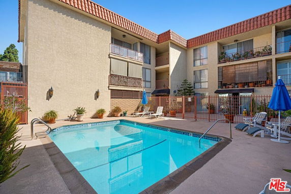 Outdoor swimming pool area with multi-story building in the background.