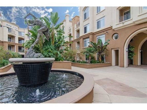 Front view of a multi-story residential building with an ornate fountain and greenery.