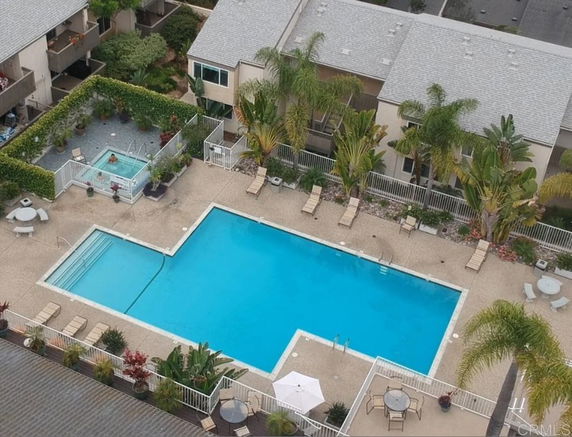 Aerial view of a swimming pool area with lounge chairs, surrounding buildings, and a smaller spa pool.