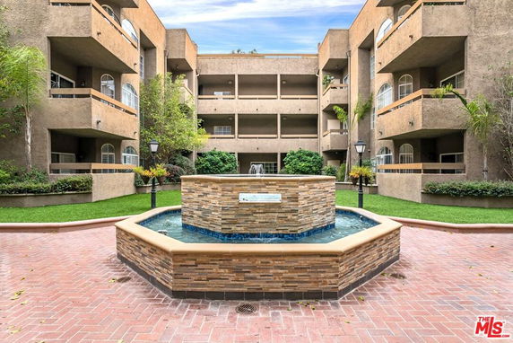 Front view of a multi-story apartment building with balconies and a central courtyard fountain.