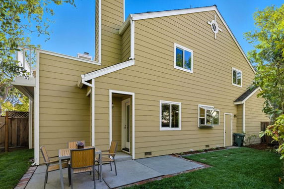View of a two-story house with a patio and table in the backyard.