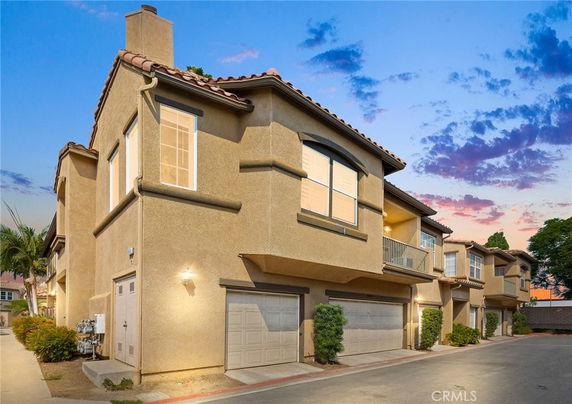 Front view of a multi-story residence with a garage at the ground level under evening skies.