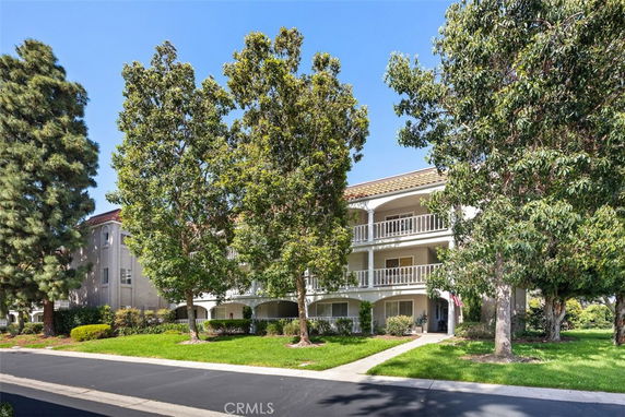 Front view of a three-story residential building with balconies and surrounding trees.