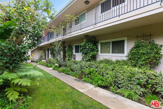Front view of a two-story residential building with a walkway and surrounding greenery.