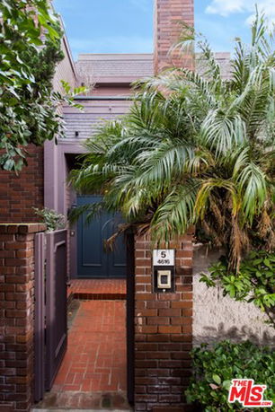 Front view of a brick house with a wooden gate and a plant beside the entrance.