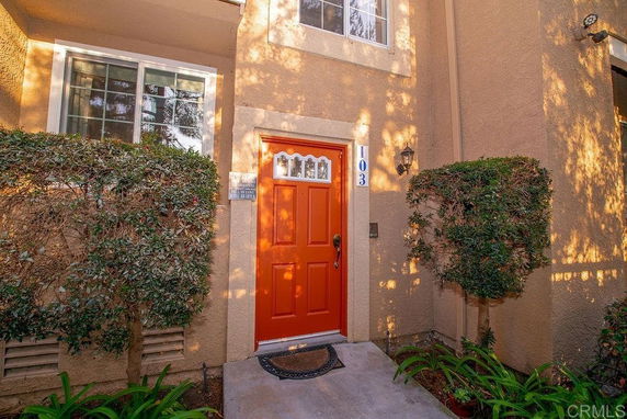 Front view of a house with a prominent red door and surrounding greenery.