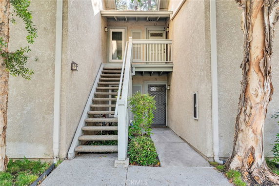 Entryway view of a multi-story building with external stairs leading to a door and balcony.