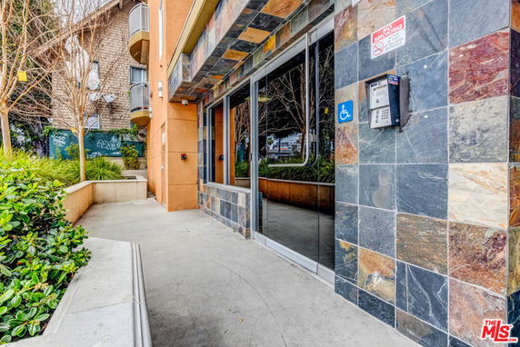 Entrance view of a multi-story building with stone tile facade and an access control system.