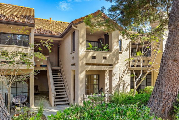 Front view of a two-story residential building with a staircase leading to the upper level and a small patio.