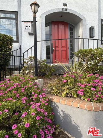 Front view of a house with a red door and garden flowers.