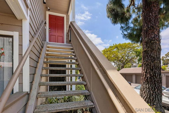 Front view of an upper-level entrance with a red door and stairs leading up.