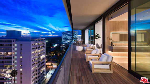 Modern apartment balcony with seating area overlooking the city skyline at dusk.