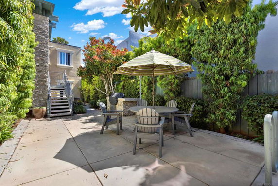 Outdoor patio area with seating and umbrella near a house with stone facade and external staircase.