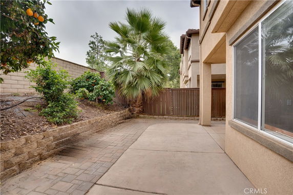 Side view of a building with a patio and nearby vegetation, including orange trees and a palm tree.