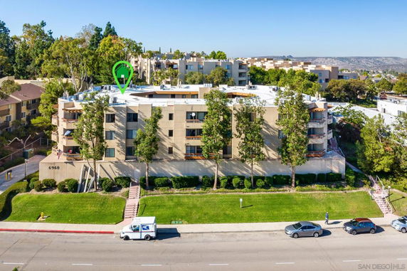 Front view of a multi-story apartment building with balconies and surrounded by trees.