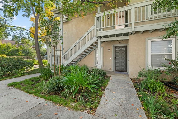 Front view of a two-story house with an exterior staircase and a small garden area.