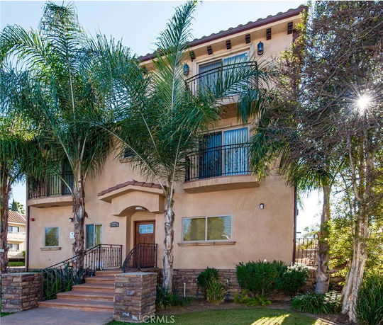 Front view of a multi-story residential building with balconies and a staircase entrance.