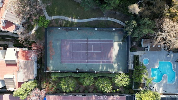 Aerial view of a tennis court surrounded by trees and adjacent buildings.