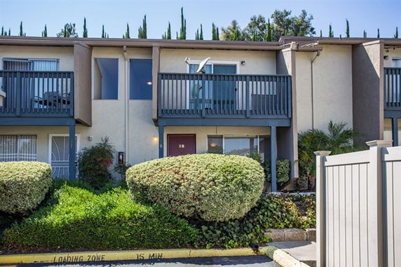 Front view of a two-story townhouse with balconies and shrubs in front.