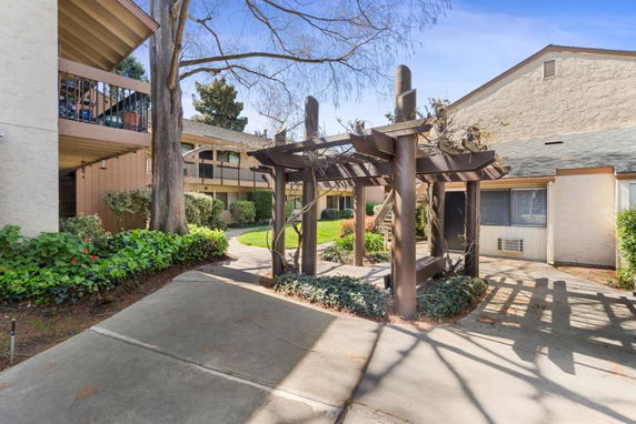 Exterior view of a residential building with a wooden pergola and landscaped pathways.