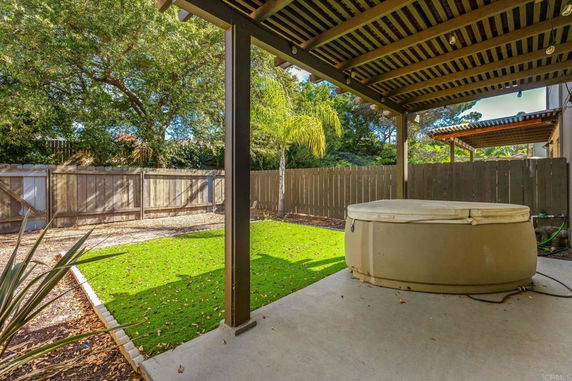 Outdoor view of a fenced backyard with a covered patio and a hot tub.