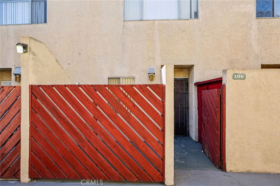 Front entrance of a building with a red diagonal wooden fence and beige stucco walls.