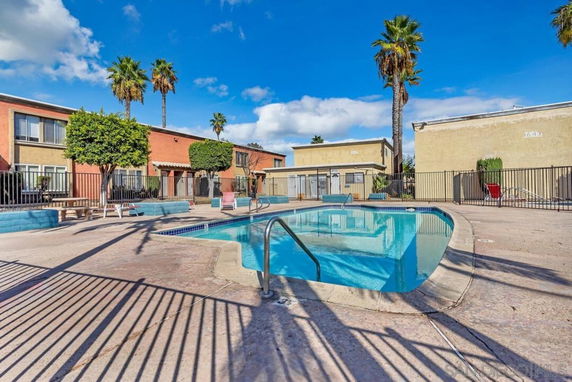 Outdoor area with a fenced swimming pool surrounded by multi-story buildings and palm trees.
