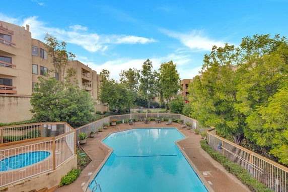 Outdoor swimming pool area surrounded by trees and apartment buildings.