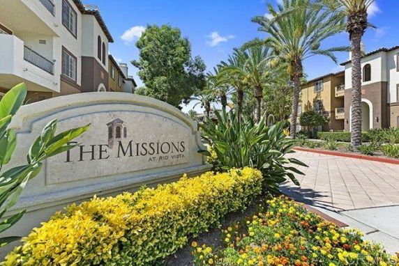 Front view of a multi-story apartment complex with palm trees and signage in the foreground.