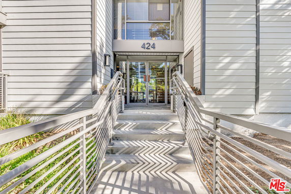 Front view of a modern building entrance with a metal railing and glass doors.