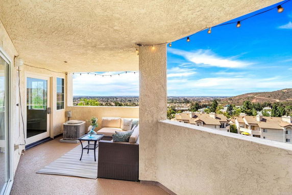 Covered balcony with outdoor seating and panoramic view of buildings and hills.