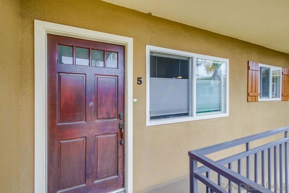 Front view of a beige house with a dark wooden door and adjacent windows.