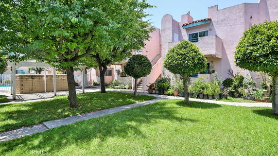 Front view of a two-story pink building with a balcony and surrounding greenery.