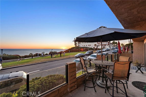 Outdoor seating area on a patio with a view of the ocean and a road.