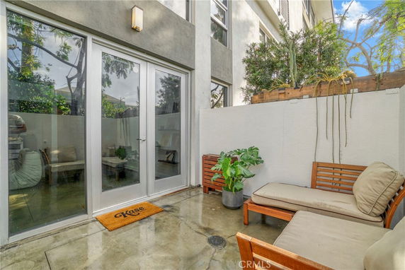 Outdoor patio area with seating and potted plants next to a building with large glass doors.