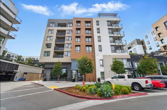 Front view of a multi-story residential building with balconies and a parking area in front.