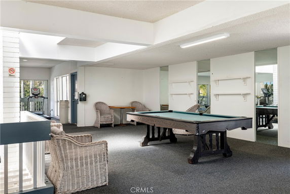 Room with a pool table, wicker chairs, and exercise equipment.